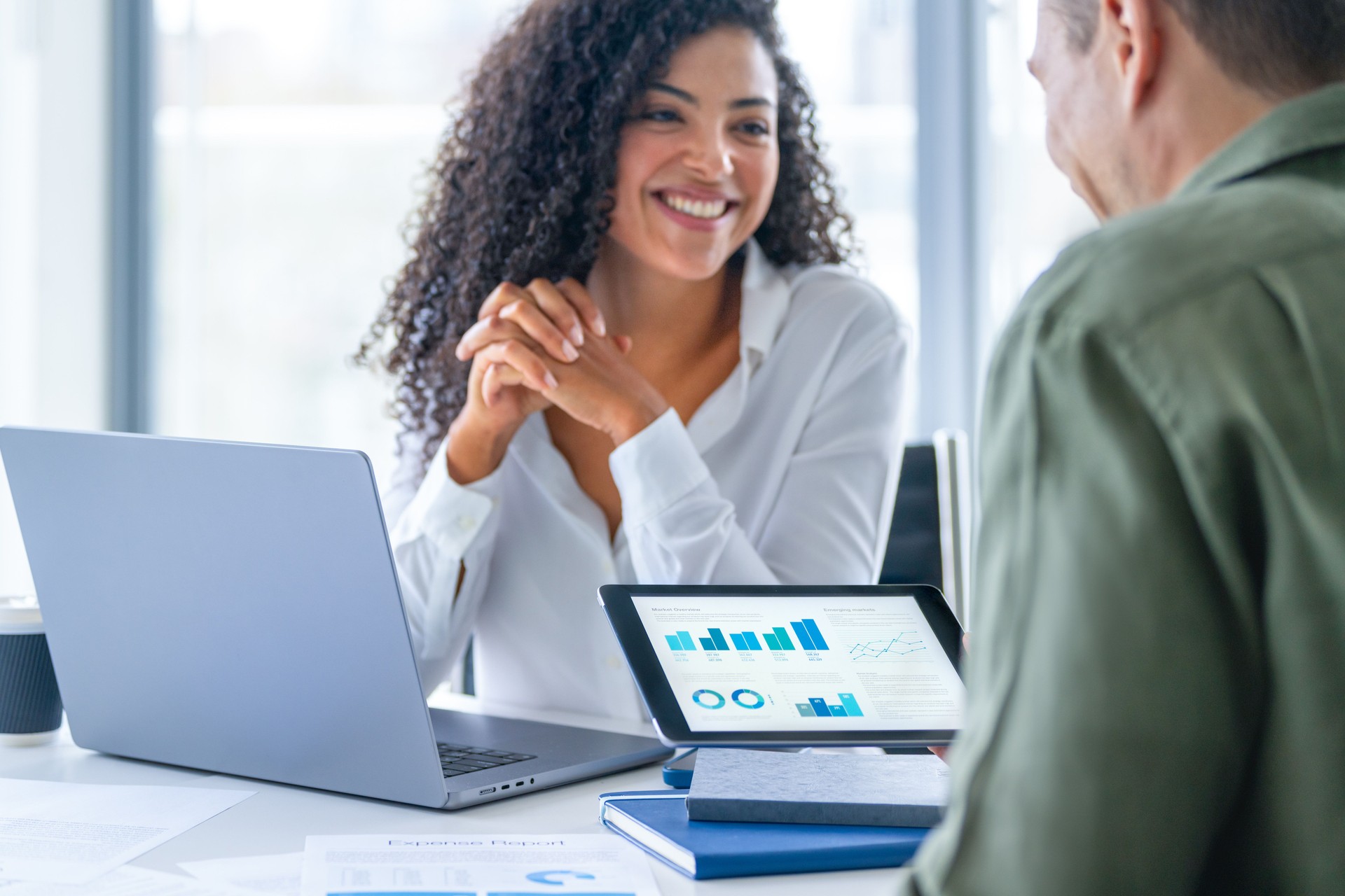 Business man and business woman in a meeting at the office. There is a laptop on the table and the man is holding a digital tablet with finance chart and graphs Business man and business woman in a meeting at the office. There is a laptop on the table and the man is holding a digital tablet with finance chart and graphs